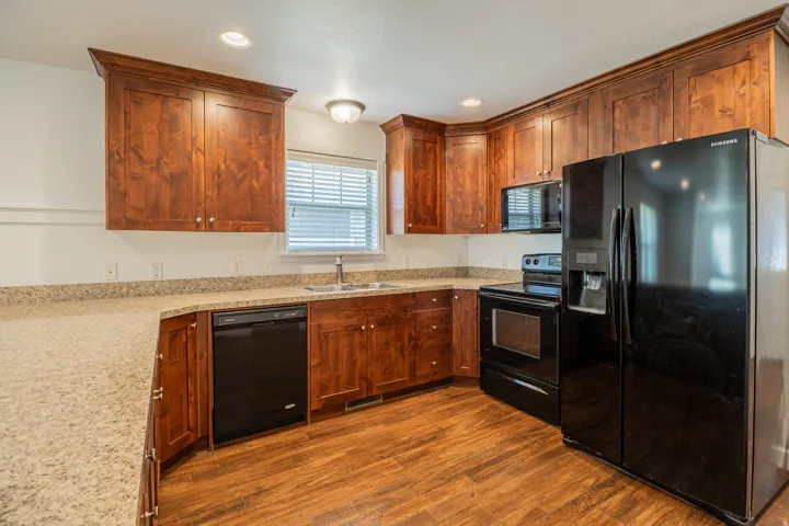 Kitchen featuring wood-finish flooring, wood cabinetry with crown molding, light-toned countertops, and black appliances