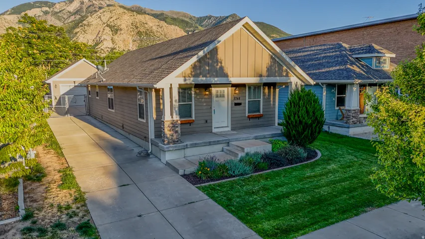 Front exterior with stone accent columns, a gabled roofline, a concrete driveway, a separate garage structure, and mountain backdrop