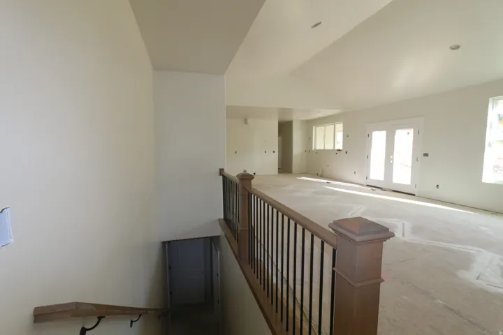 Spacious interior with vaulted ceilings, natural light from multiple windows, and a wood-finish newel post and handrail with black iron balusters