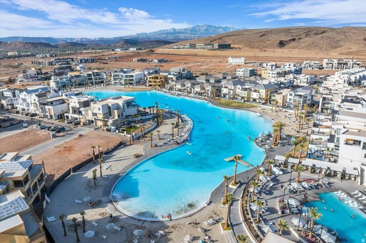 Expansive community featuring a large aquatic amenity with sandy shores and multiple swimming areas, surrounded by contemporary multi-story residences
