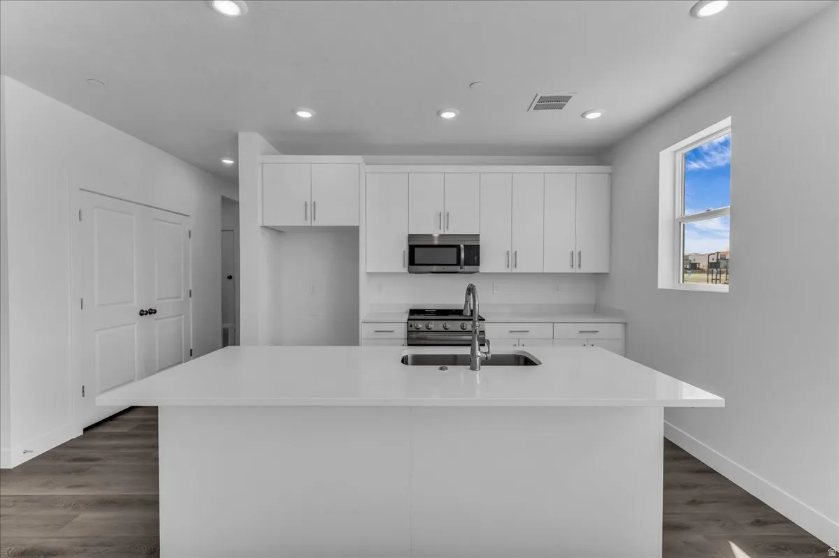Modern kitchen featuring an expansive island with an undermount sink, white cabinetry with stainless steel hardware, recessed lighting, and wood-finish flooring