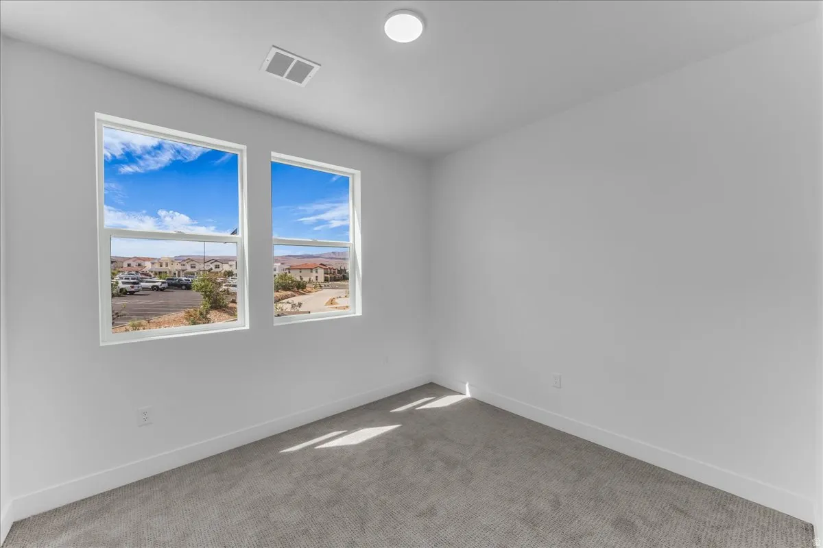 Bright room featuring two large windows, grey carpeting, a ceiling-mounted light fixture, and white walls