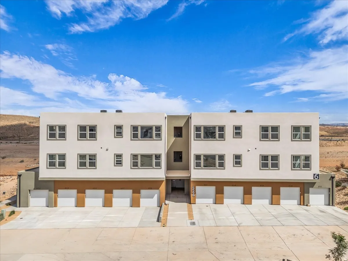 Contemporary multi-story exterior with a stucco finish, multiple individual garage doors, and a desert landscape backdrop