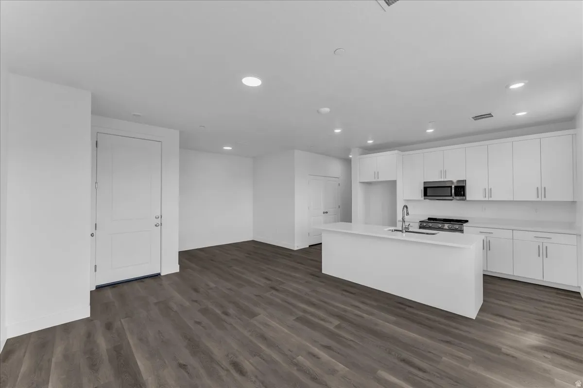 Open-concept living space with wood-finish flooring, recessed lighting, and a kitchen featuring a central island, white cabinetry, and stainless steel appliances