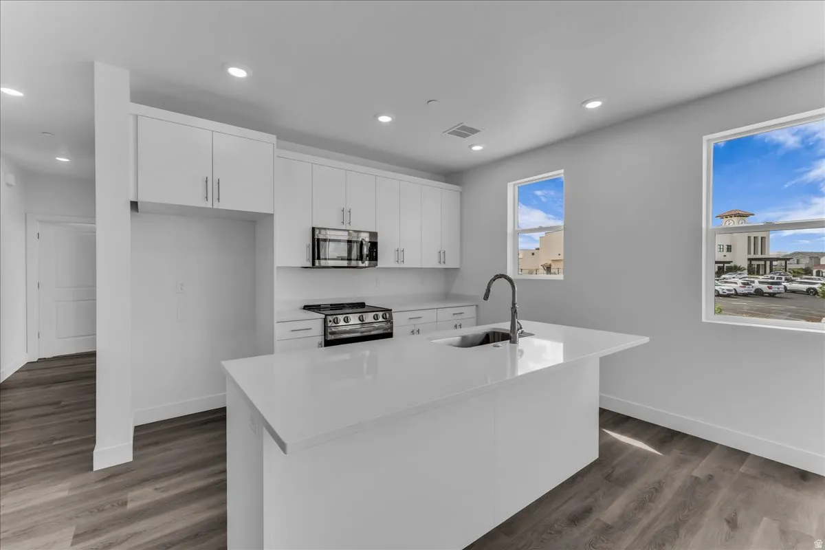 Contemporary kitchen featuring white cabinetry, a large center island with an integrated sink, stainless steel appliances, and wood-finish flooring