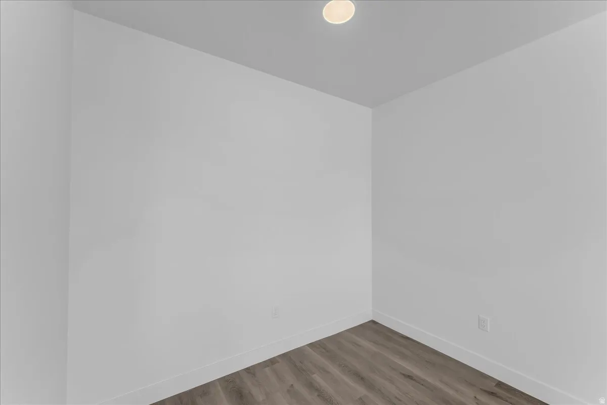Recessed ceiling light, neutral wall paint, wood-finish flooring, and white baseboards