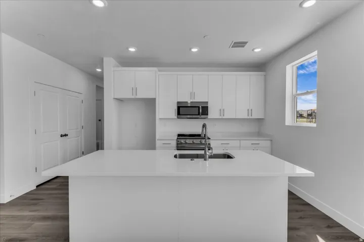 Modern kitchen featuring an expansive island with an undermount sink, white cabinetry with stainless steel hardware, recessed lighting, and wood-finish flooring
