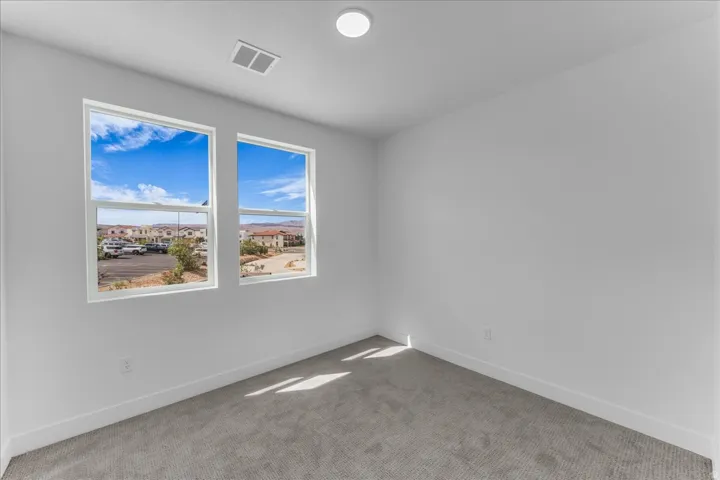 Bright room featuring two large windows, grey carpeting, a ceiling-mounted light fixture, and white walls