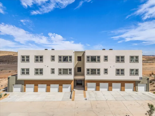 Contemporary multi-story exterior with a stucco finish, multiple individual garage doors, and a desert landscape backdrop