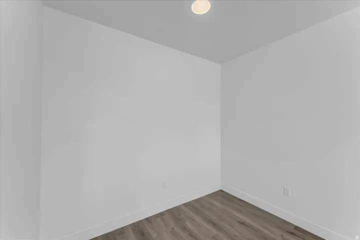 Recessed ceiling light, neutral wall paint, wood-finish flooring, and white baseboards