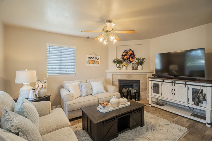 Fireplace with tile surround and mantel, corner placement, ceiling fan with light fixture, wood-finish flooring, window with blinds