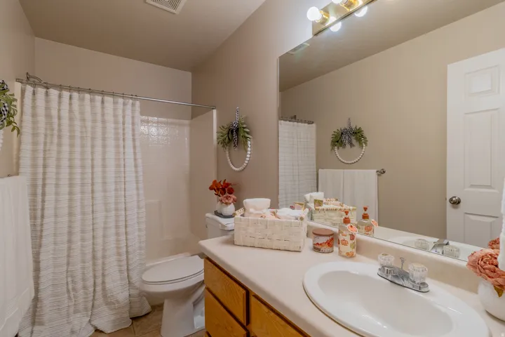 Bathroom featuring a built-in vanity with an integrated sink, a large wall-mounted mirror, and a shower with a tiled surround