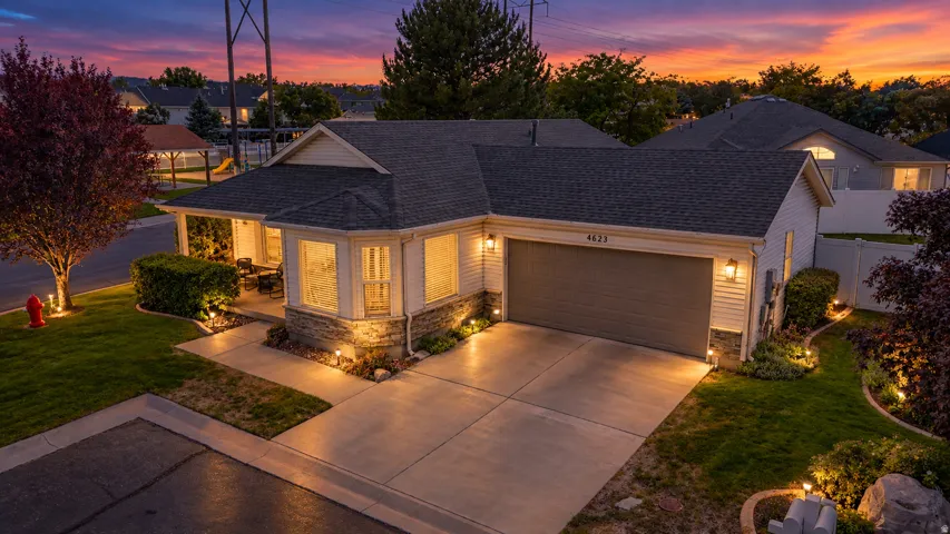 Exterior with siding and stone accents, an attached garage, a covered front porch, and established landscaping with accent lighting