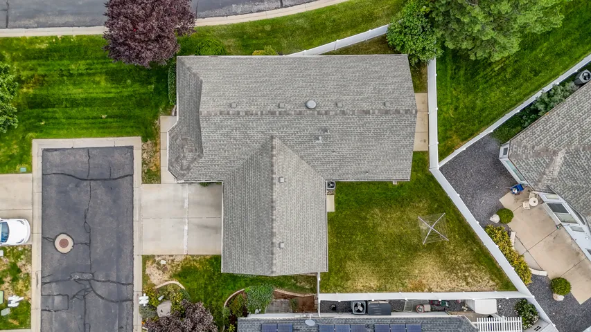 Gable roofline with asphalt shingles, expansive green lawn, concrete driveway, white privacy fencing, and mature landscaping