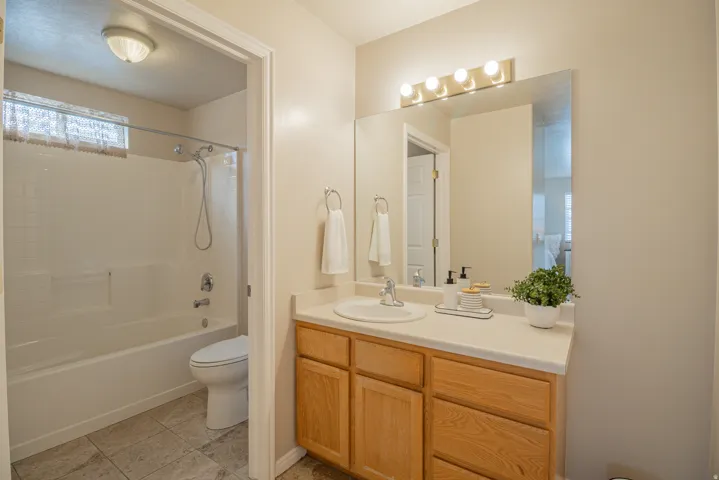 Full bathroom featuring a vanity with a light wood-finish cabinet and white countertop, an integrated sink with a chrome faucet, a large wall-mounted mirror, and a combination shower and tub with white tile surround
