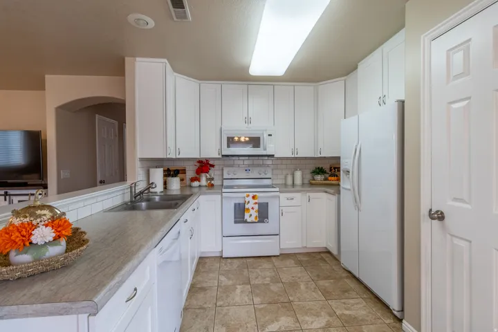 White cabinetry, subway tile backsplash, stainless steel sink, integrated dishwasher, and tile flooring