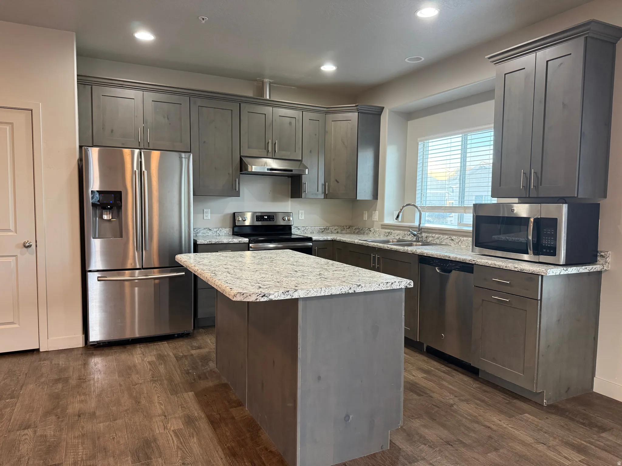 Kitchen featuring wood-finish flooring, gray cabinetry, stainless steel appliances, a kitchen island, and light-toned countertops