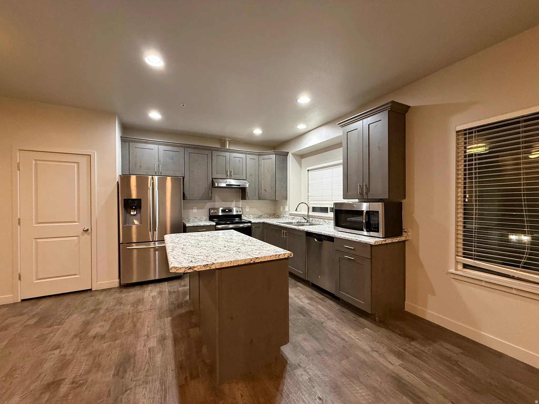 Kitchen featuring wood-finish flooring, gray cabinetry, granite countertops, and stainless steel appliances