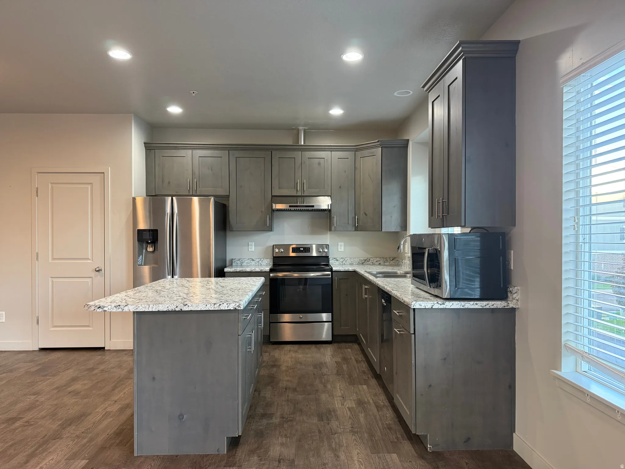 Kitchen featuring wood-finish flooring, recessed lighting, gray cabinetry, light-toned countertops, and stainless steel appliances