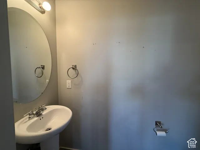 Pedestal sink with chrome faucet, circular wall mirror, and chrome vanity light