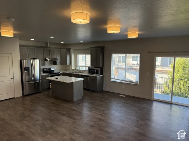 Open-concept living space with wood-finish flooring, a kitchen island, stainless steel appliances, and sliding glass door access to an exterior balcony