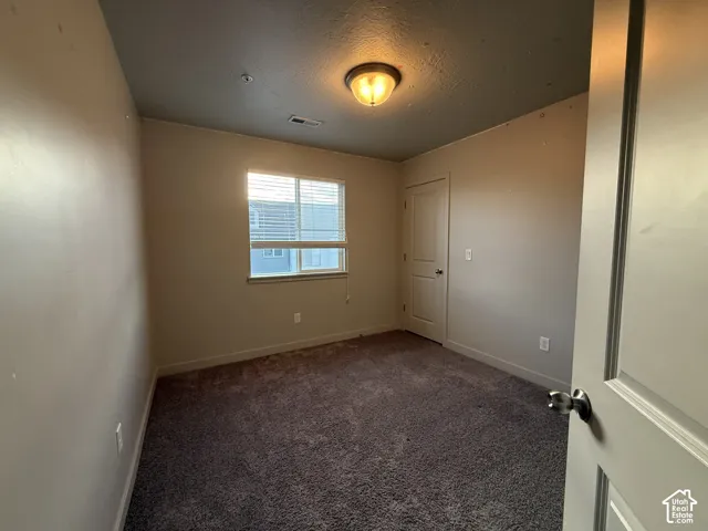 Carpeted flooring, window with blinds, interior door, flush mount ceiling light, and neutral wall tones