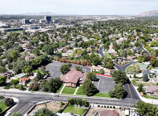Expansive property with a large paved parking area and mature trees surrounded by single family homes on three sides