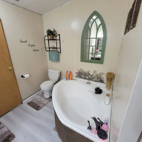 Corner soaking tub with integrated faucet, light-toned wood-finish flooring, and a wall-mounted decorative mirror