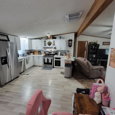 White cabinetry, stainless steel appliances, light wood-finish flooring, and a tiled backsplash