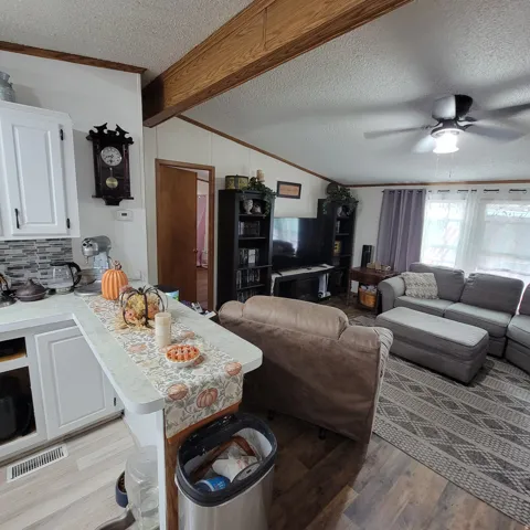 Wood-finish flooring throughout, white cabinetry with dark hardware, a tile backsplash, and exposed ceiling beams
