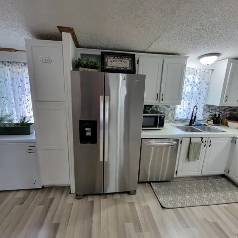 Stainless steel side-by-side refrigerator, white cabinetry, wood-finish flooring, undermount dual-basin sink, and tile backsplash