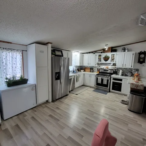 Kitchen featuring stainless steel appliances, white cabinetry, a tiled backsplash, and wood-finish flooring