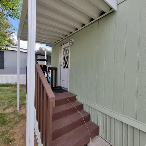 Covered entryway featuring a paneled door with diamond-patterned glass, exterior wall lighting, and wood-finish steps with railing