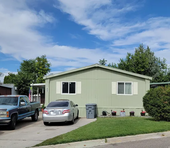 Light green exterior siding with white window trim and shutters, front yard with mature landscaping, and an asphalt driveway