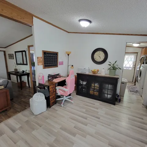 Wood-finish flooring with varying tones, overhead flush mount lighting, crown molding, and a built-in wood-look desk