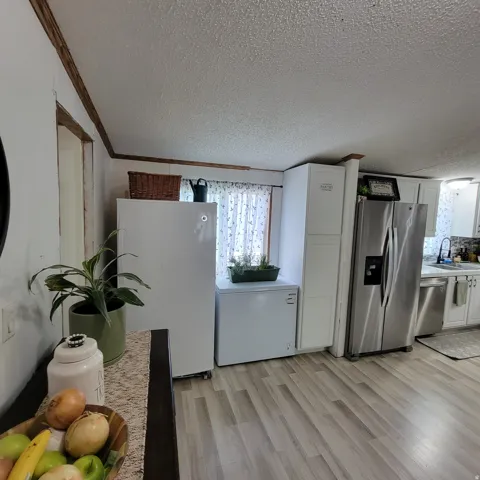 Wood-finish flooring, white cabinetry, stainless steel appliances, and a window with sheer curtains