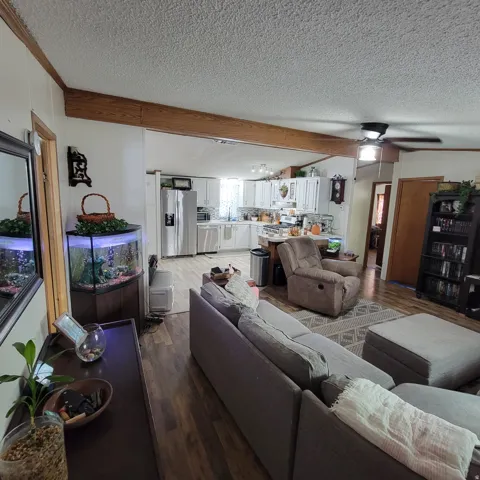Open-concept living area featuring wood-finish flooring, a ceiling fan with integrated lighting, and a prominent wood beam detail