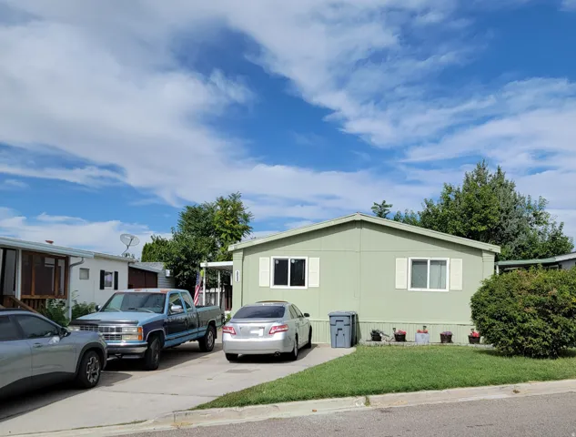 Pale green siding exterior with white window trim and shutters, concrete driveway, and a manicured lawn