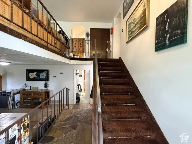 Multi-level interior featuring a carpeted staircase with metal accents, flagstone flooring, and an open loft area with wrought iron railings