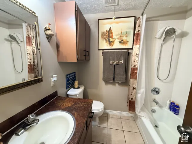 Bathroom featuring a single vanity with a white basin sink, a brown-toned countertop, overhead cabinetry, and a shower-tub combination