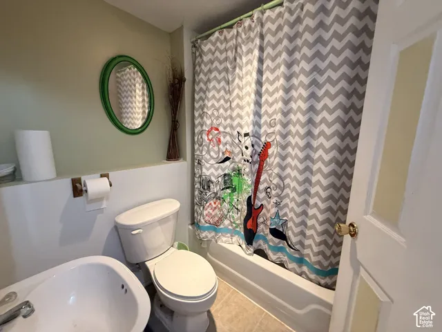 White porcelain toilet, white bathtub, and light-toned floor tiling