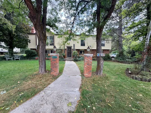 Siding exterior with brick architectural elements, mature trees, and a concrete walkway