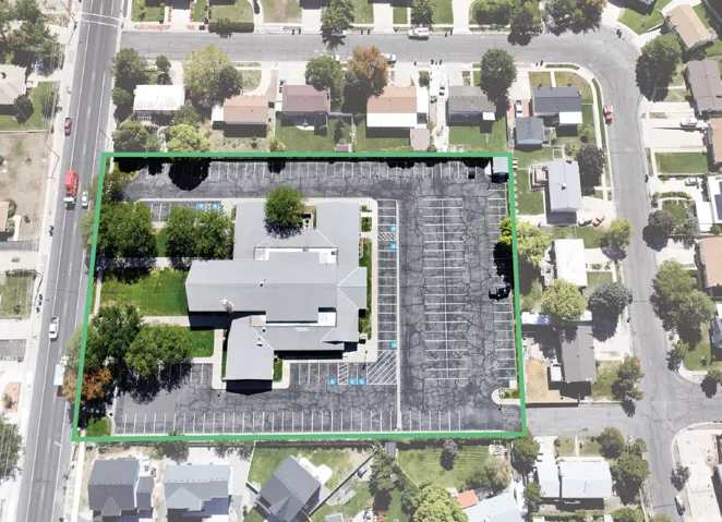 Expansive lot featuring a large building with a multi-gabled roof, extensive asphalt parking, and mature trees