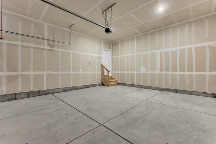 Concrete flooring, unfinished drywall, interior door, wooden staircase, overhead garage door opener