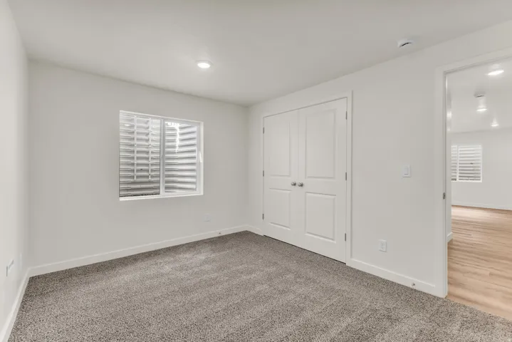 Recessed lighting illuminates the room, featuring a carpeted floor, white walls, and a window with a window well