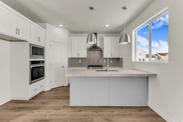 Contemporary kitchen featuring white cabinetry, integrated stainless steel appliances, a light-toned countertop, and wood-finish flooring