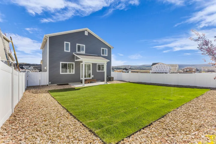 Two-story residence with dark siding, white trim windows, covered patio, green lawn, and rock landscaping
