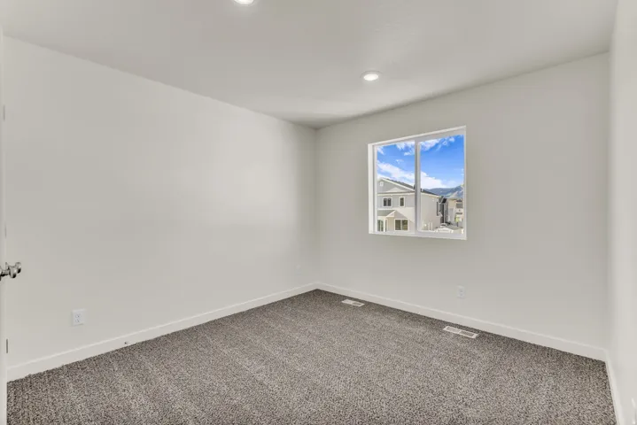 Bright room featuring a window with white framing, recessed ceiling lighting, and gray carpeting