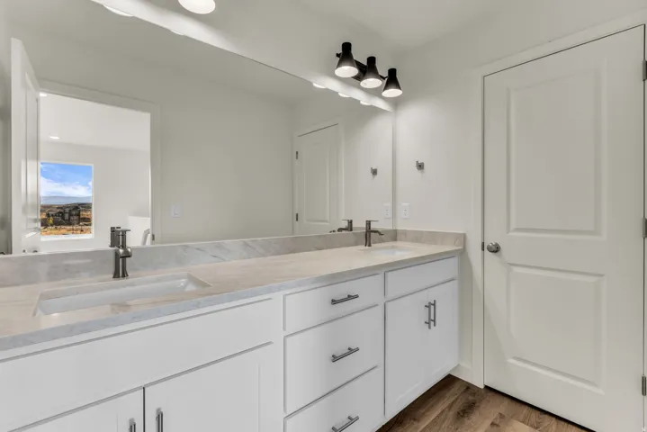 Dual vanity with integrated sinks, light-toned countertop, white cabinetry with contemporary hardware, and wood-finish flooring
