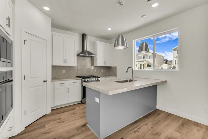 Kitchen featuring wood-finish flooring, white cabinetry, integrated stainless steel appliances, a center island with sink, and pendant lighting